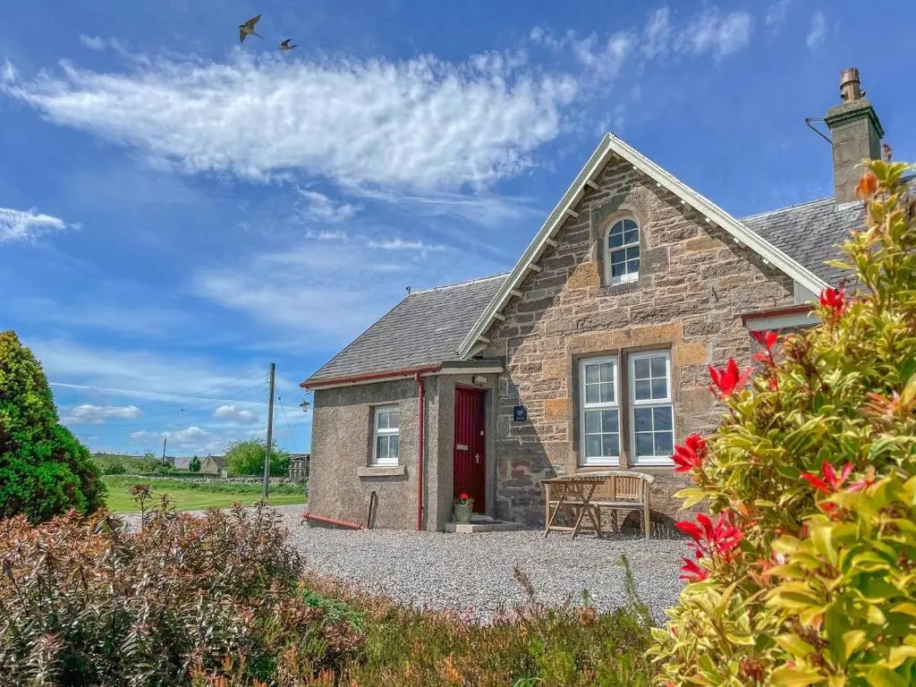 a stone house with a red door and flowers at Rowan Cottage - Uk38991 in Dalcross
