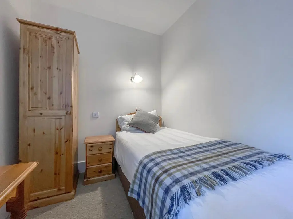 a small bedroom with a bed and a wooden cabinet at Rowan Cottage - Uk38991 in Dalcross