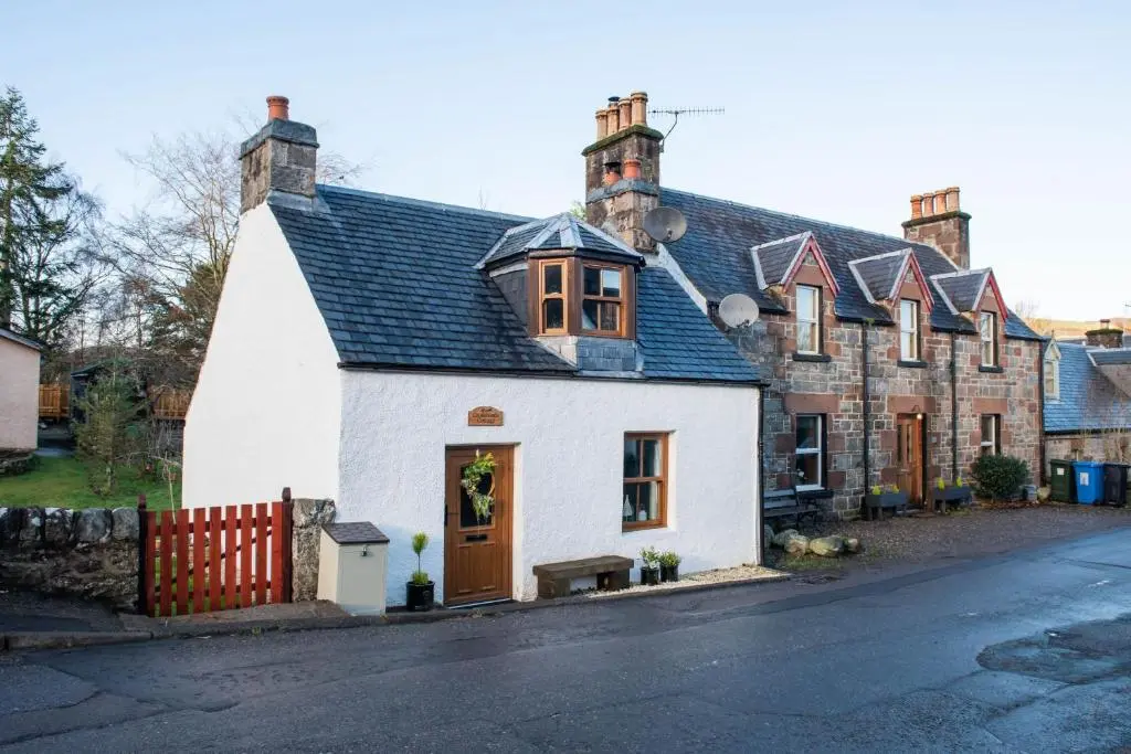 a white house with a black roof on a street at Crossroads Cottage in Drumnadrochit