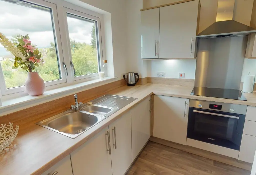 a kitchen with white cabinets and a sink and a window at 10 Bynack House in Aviemore