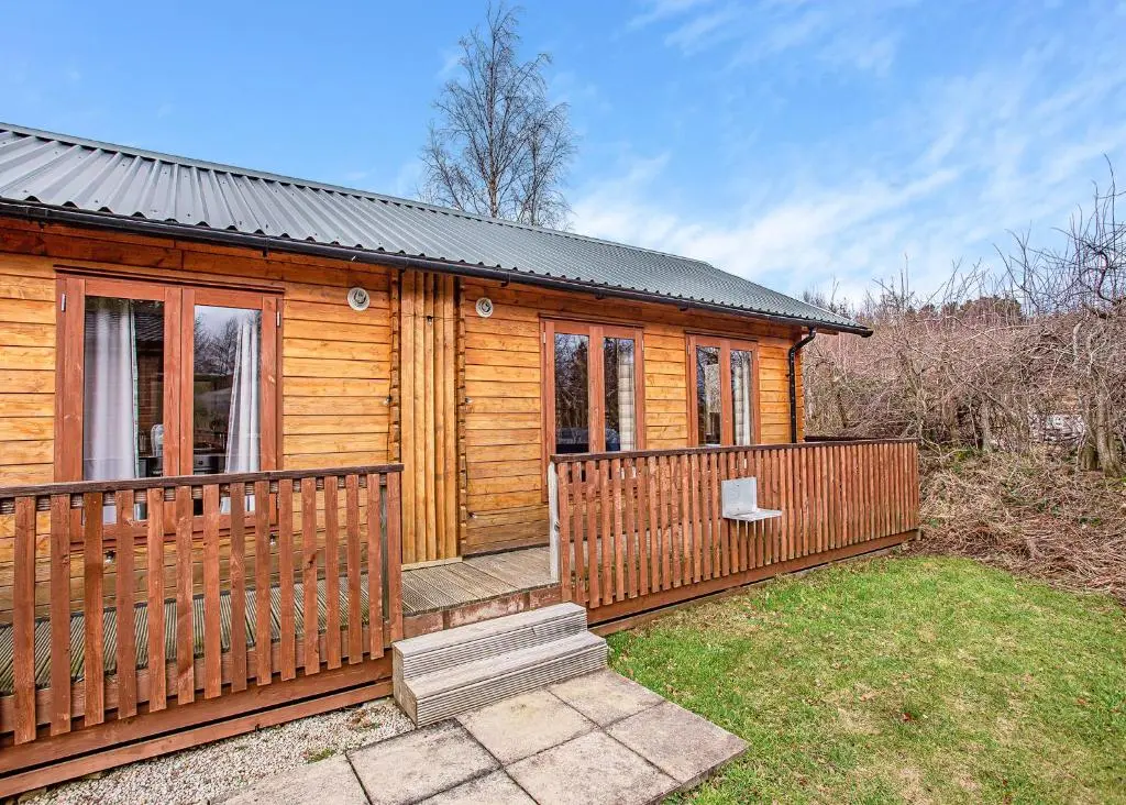 a wooden cabin with a porch and a fence at Castlewood Lodges in Strachan
