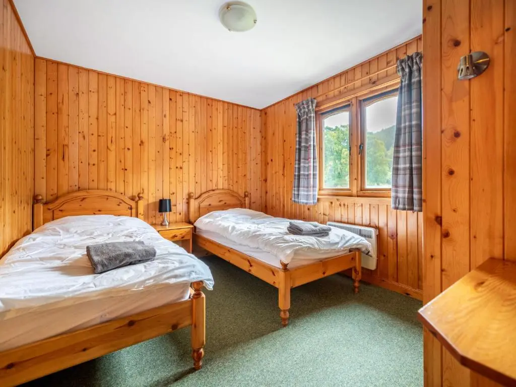 two beds in a room with wooden walls at Divach Lodge at Lochletter Lodges in Drumnadrochit