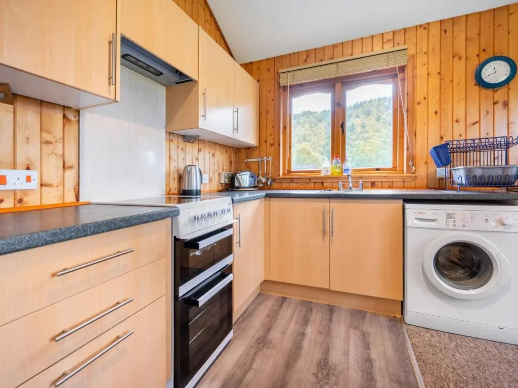 a kitchen with wooden cabinets and a washer and dryer at Divach Lodge at Lochletter Lodges in Drumnadrochit
