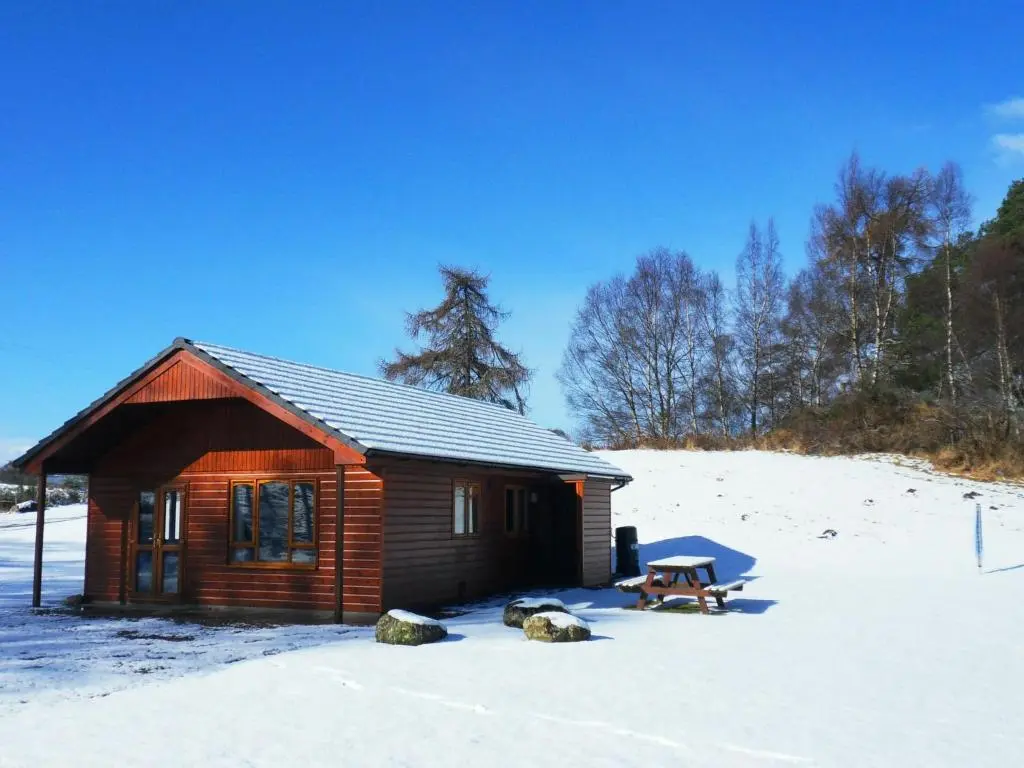 a log cabin in the snow with a picnic table at Guisachan Lodge at Lochletter Lodges in Drumnadrochit