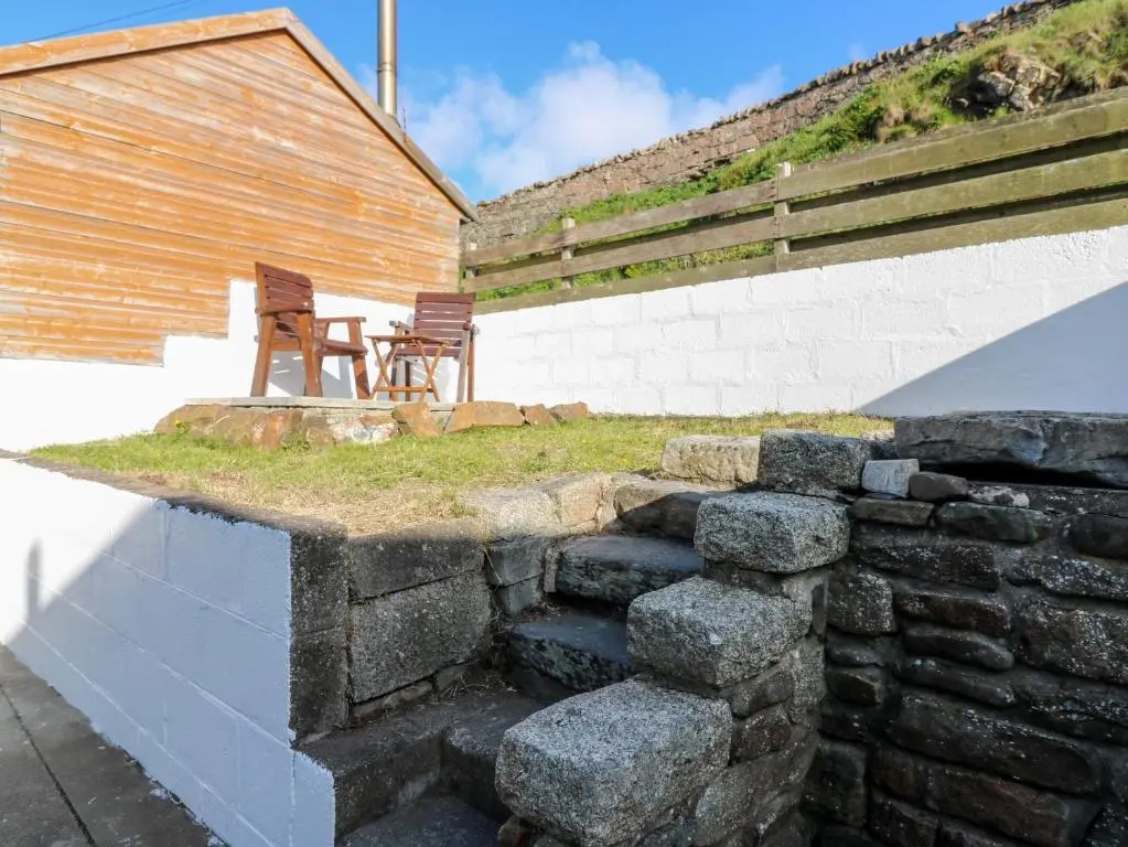 a stone retaining wall with two chairs and a table at Dolphin Cottage in Banff