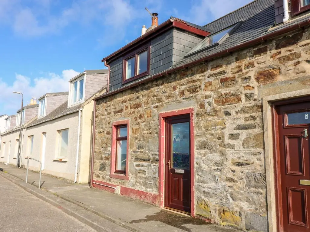 an old stone building with a red door on a street at Dolphin Cottage in Banff