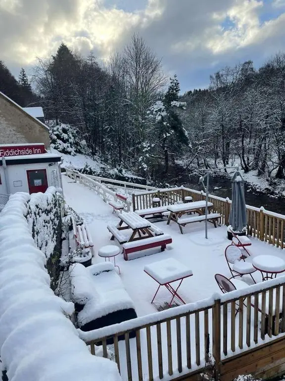 a deck covered in snow with tables and benches at The Fiddichside Inn in Aberlour