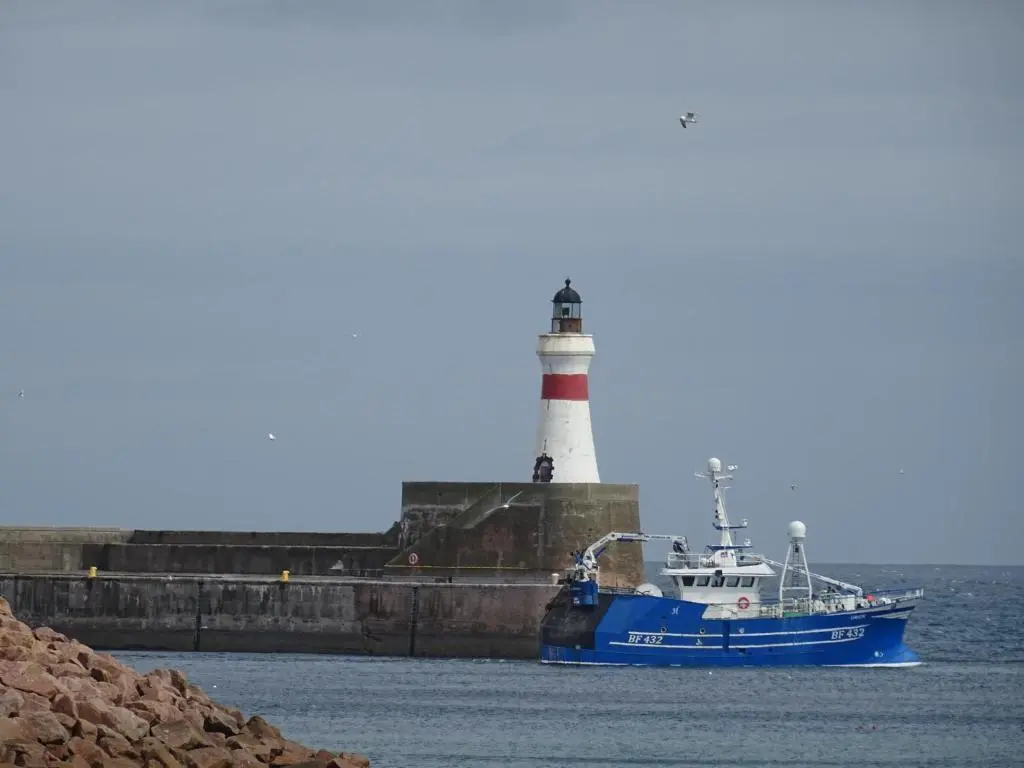 a blue boat in the water with a lighthouse at Green Yurt with Hot Tub - Sleeps 3 Parking & Pets in Turriff