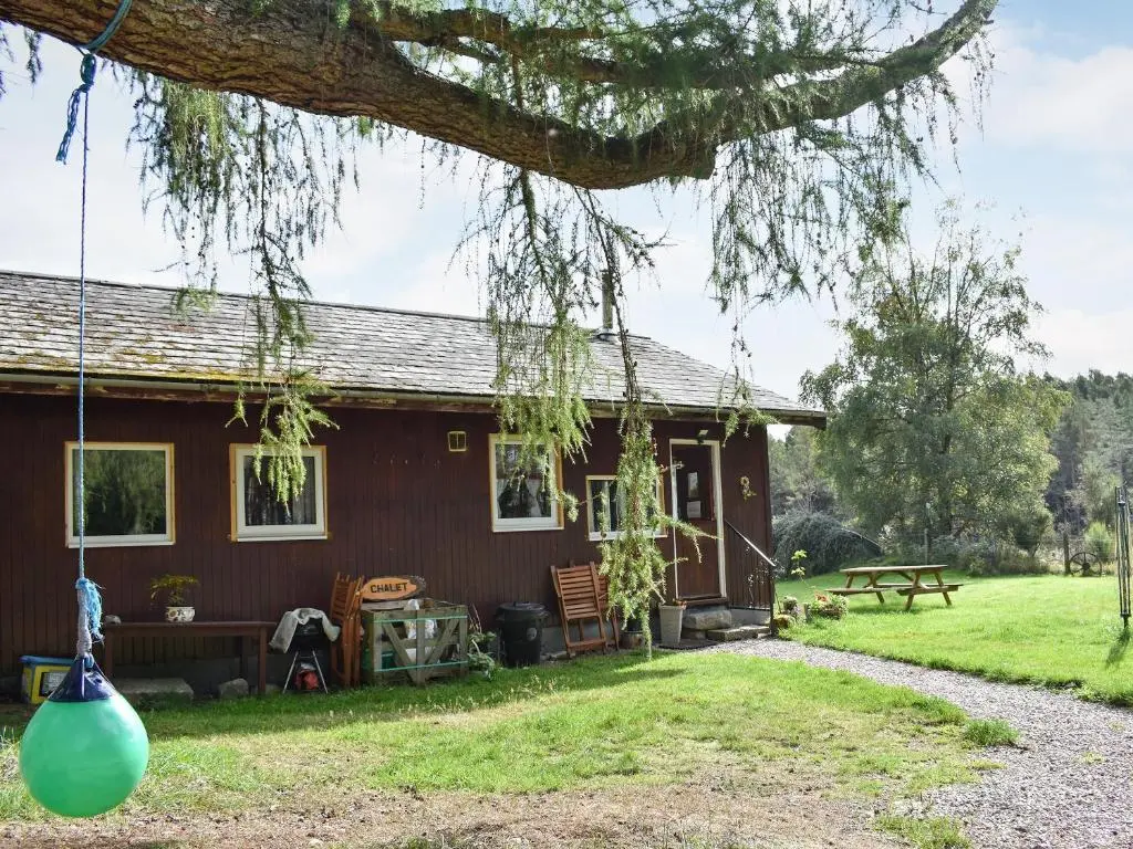 a red house with a picnic table and a bench at The Chalet - Ukc5786 in Nethy Bridge