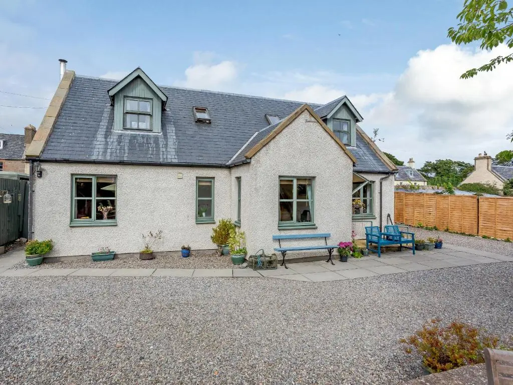 a white house with a bench and a fence at Caldon Cottage in Cromarty