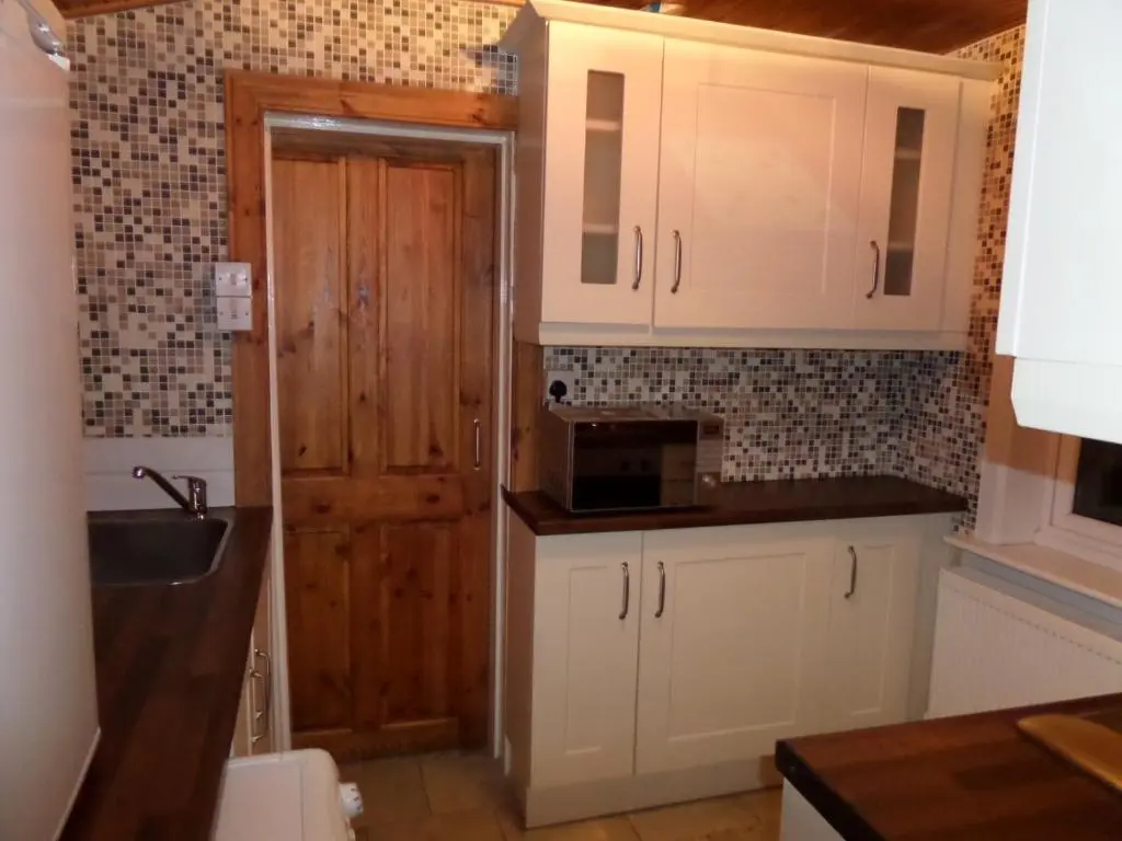 a kitchen with white cabinets and a wooden door at Jane's Cottage Free Parking in Inverness