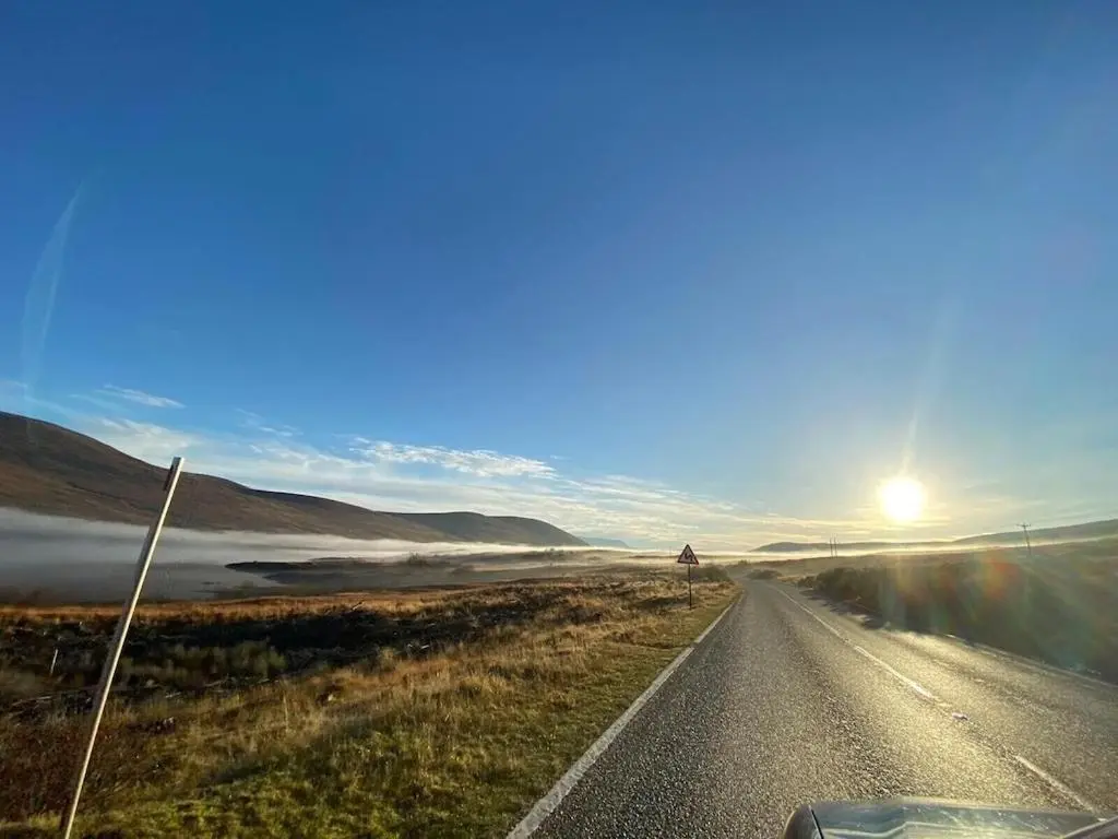 a car driving down a road with the sun in the distance at Foinaven House in Ullapool