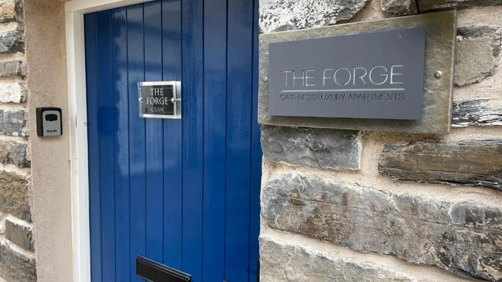 a blue door on a stone building with a sign at The Forge by Caithness Luxury Apartments NC500 - Elegant Luxury Apartment with Bike store - Sleeps 4 in Wick