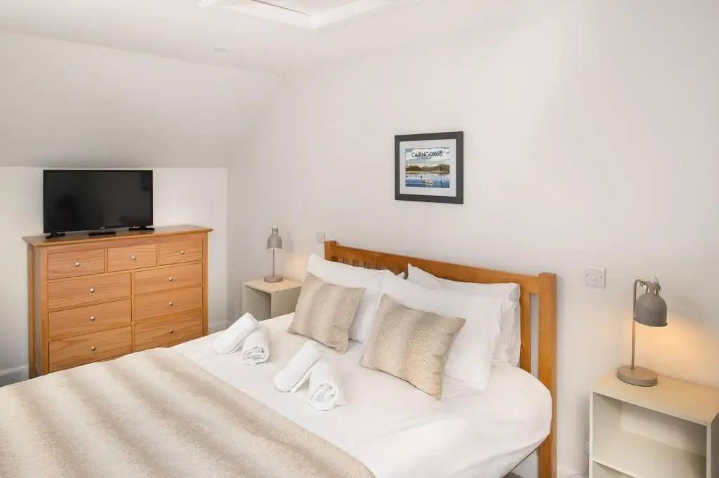 a bedroom with a white bed with a dresser and a tv at Anne's Place in Boat of Garten