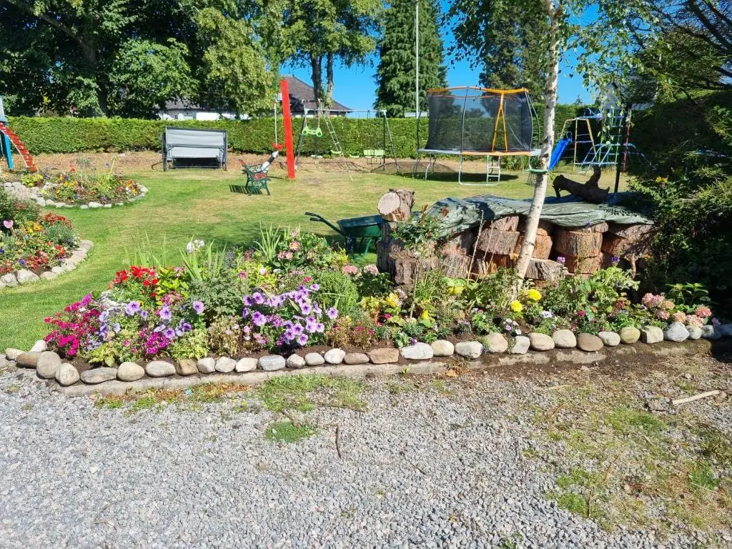 a garden of flowers in a park with a playground at Nannys tiny hoose in Inverness