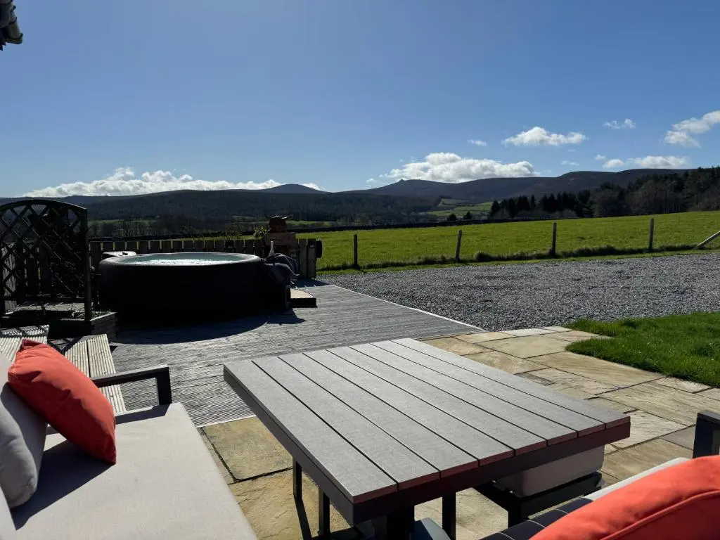 a wooden picnic table on a patio with mountains in the background at Drumhead Cottage Finzean, Banchory Aberdeenshire Self Catering with Hot Tub in Finzean