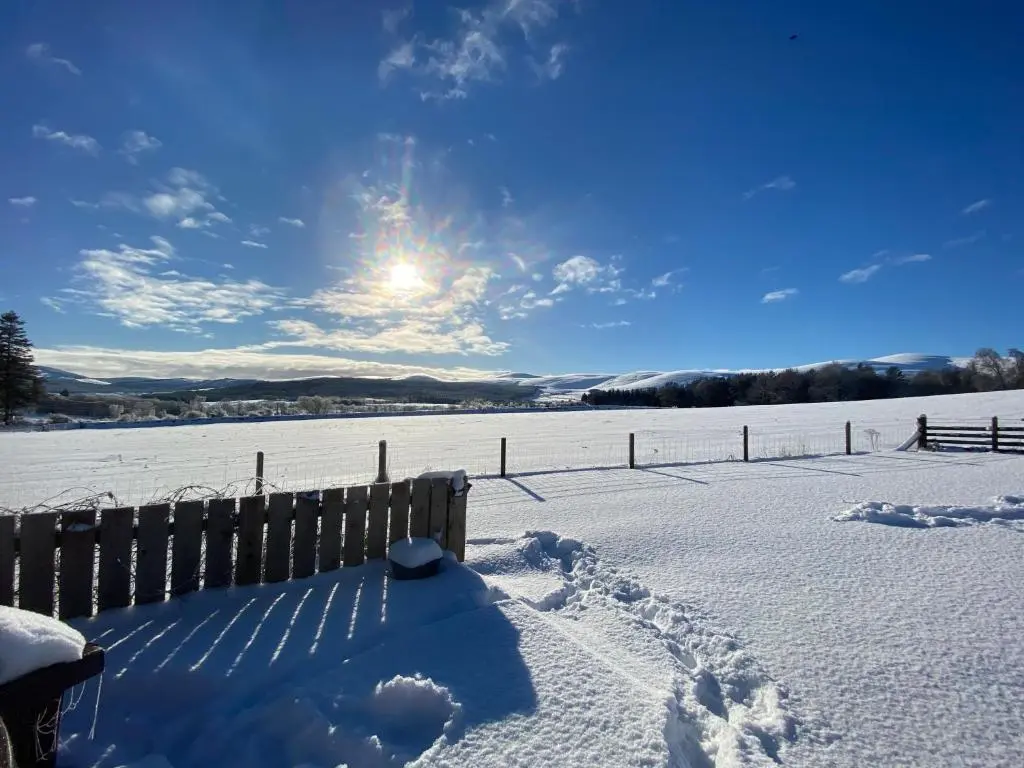 a snow covered field with the sun in the sky at Drumhead Cottage Finzean, Banchory Aberdeenshire Self Catering with Hot Tub in Finzean