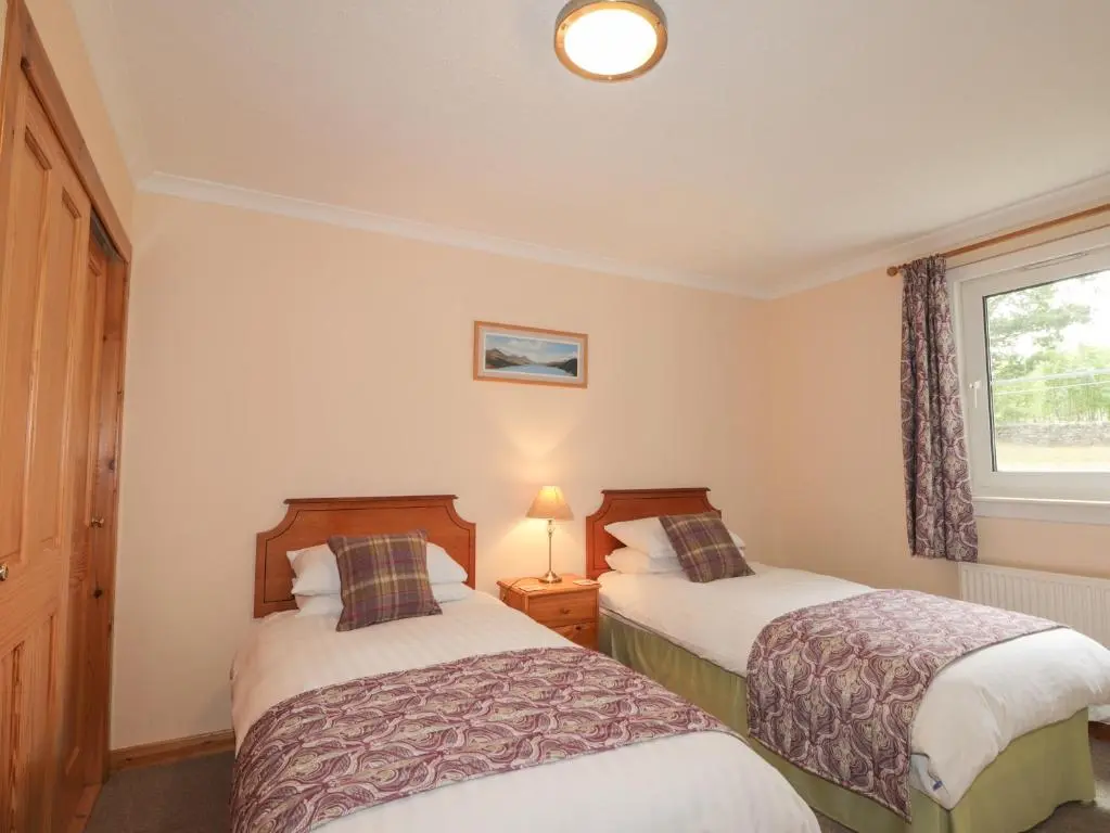 two beds in a small room with a window at Garden Lodge in Muir of Ord
