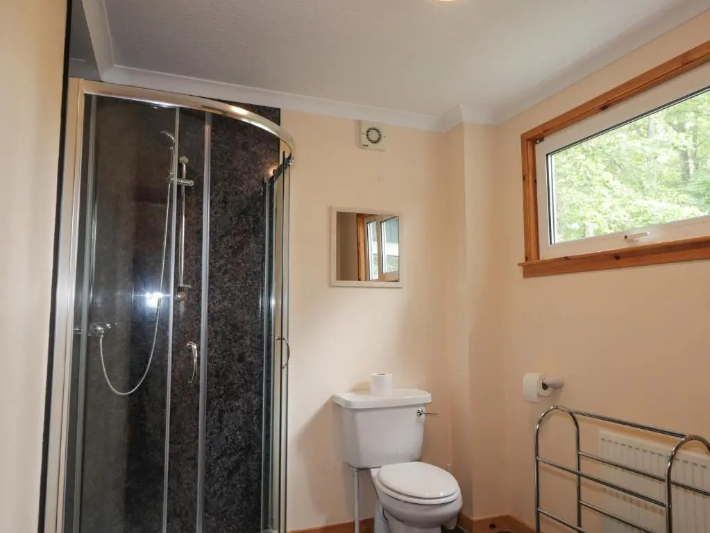 a bathroom with a shower and a toilet and a window at Garden Lodge in Muir of Ord