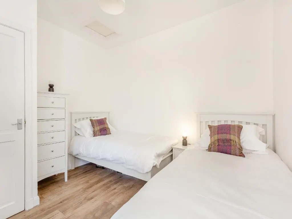 two beds in a bedroom with white walls and wooden floors at Dove Cottage in Inverness
