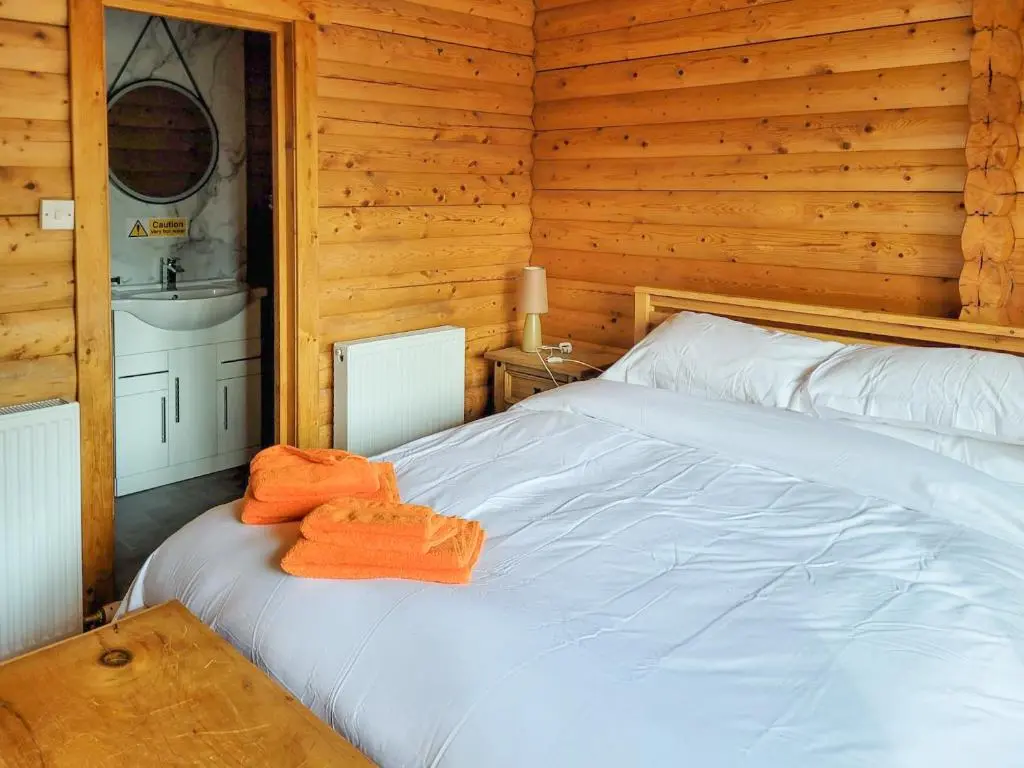 a bedroom with a white bed with orange towels on it at Ardle Lodge in Enochdhu