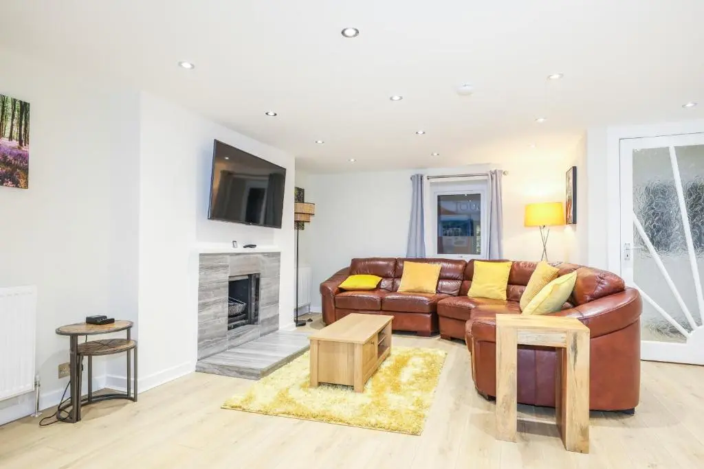 a living room with a brown leather couch and a fireplace at mySTAYINN Tomnahurich Guest House in Inverness