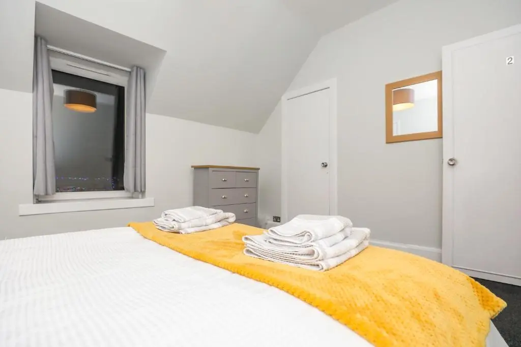 a white bedroom with a bed with towels on it at mySTAYINN Tomnahurich Guest House in Inverness
