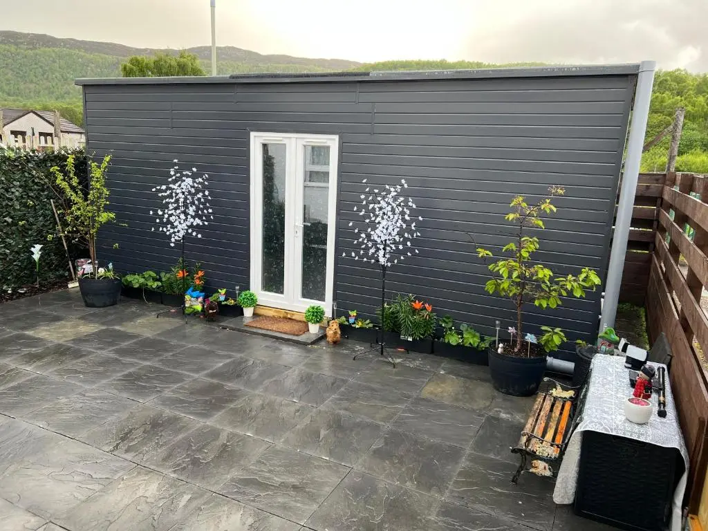 a black shed with potted plants on a patio at Craigellachie Cabin in Aviemore