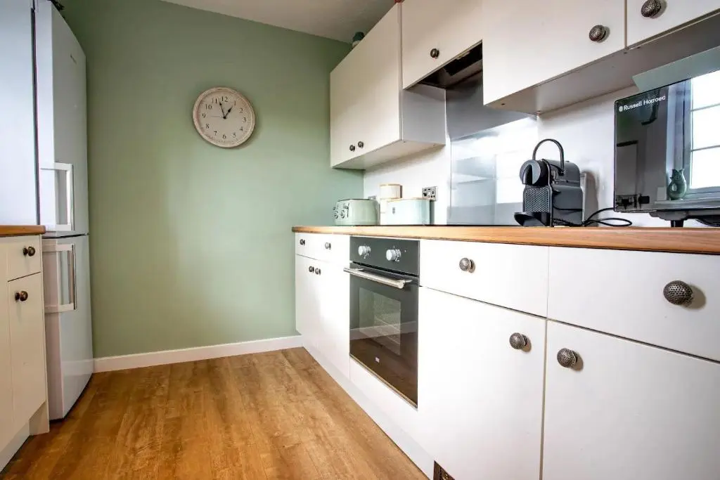 a kitchen with white cabinets and a clock on the wall at Apartment No16 in Inverness