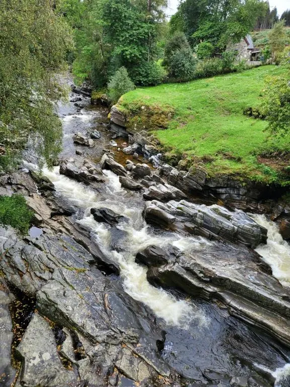 a stream of water with rocks in a field at Summer Breeze in Aviemore