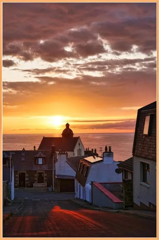 a sunset over the ocean with houses and roofs at Moray View, Macduff, Aberdeenshire. in Macduff