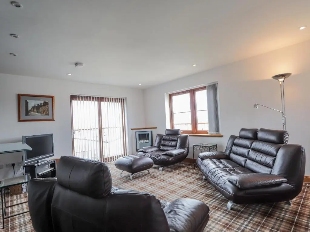 a living room with leather furniture and a television at Lossiemouth Bay Cottage in Lossiemouth