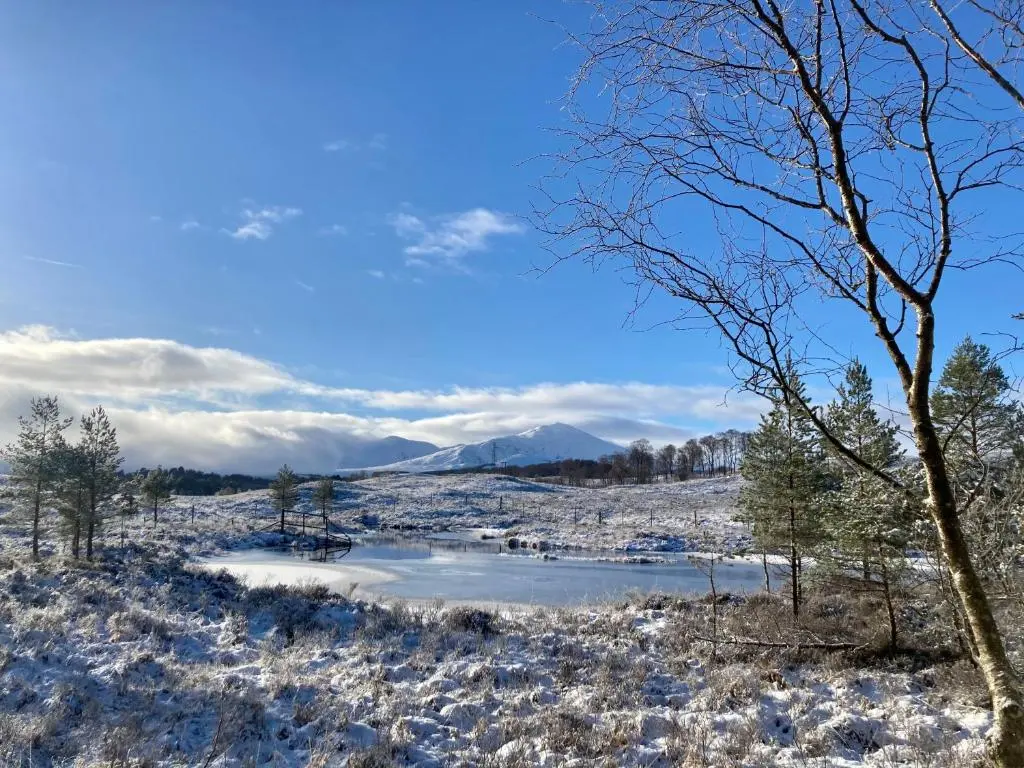 a snowy field with a pond in the foreground at Great Glen Hostel in Spean Bridge