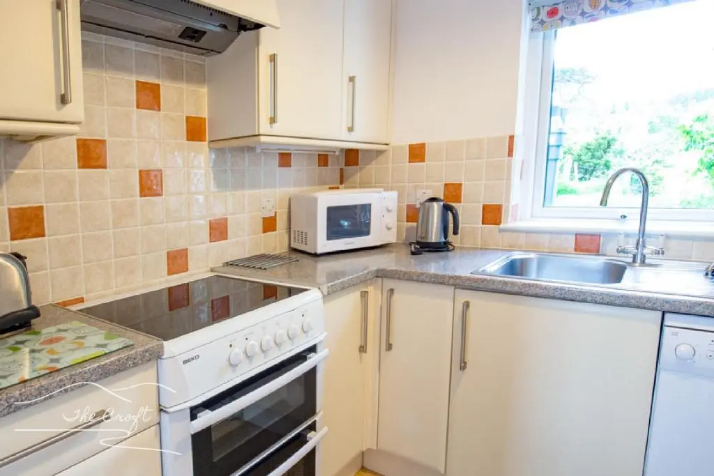 a kitchen with white cabinets and a sink and a microwave at The Croft Cottage - near Aviemore in Aviemore