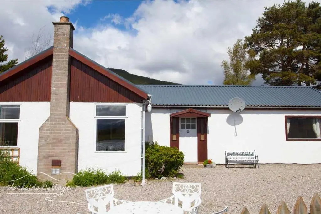 a white house with a brick building and chairs at Lochside Cottage - near Aviemore in Aviemore