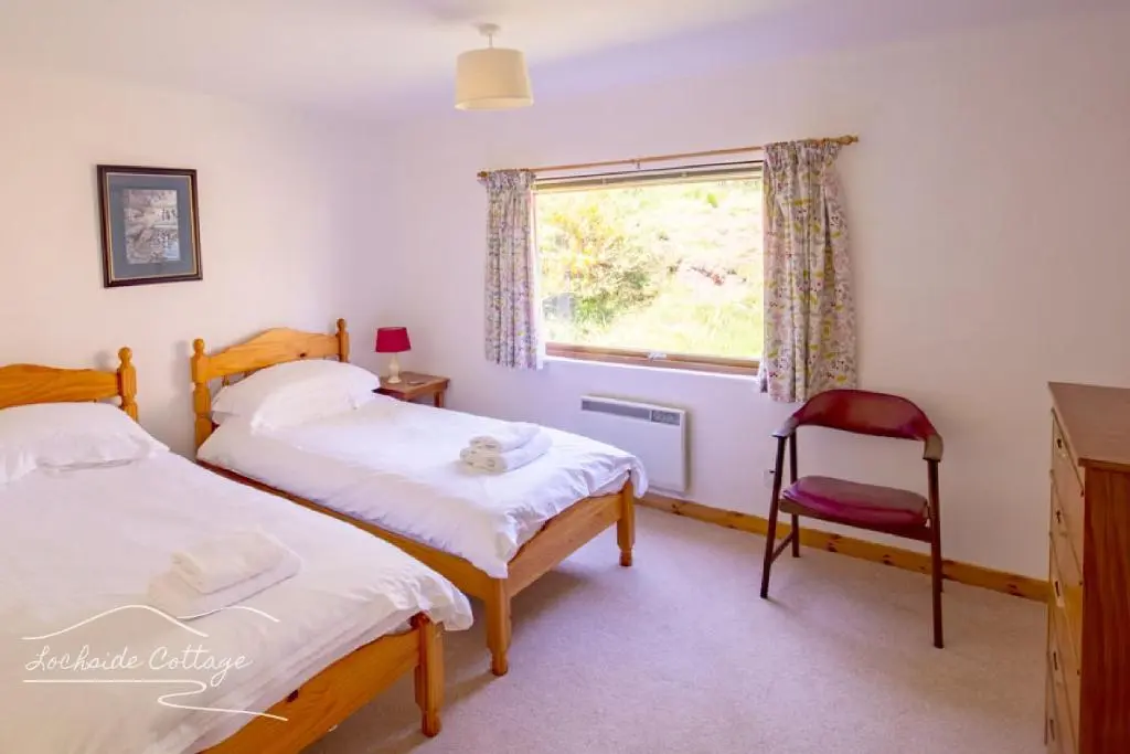 a bedroom with two beds and a red chair at Lochside Cottage - near Aviemore in Aviemore