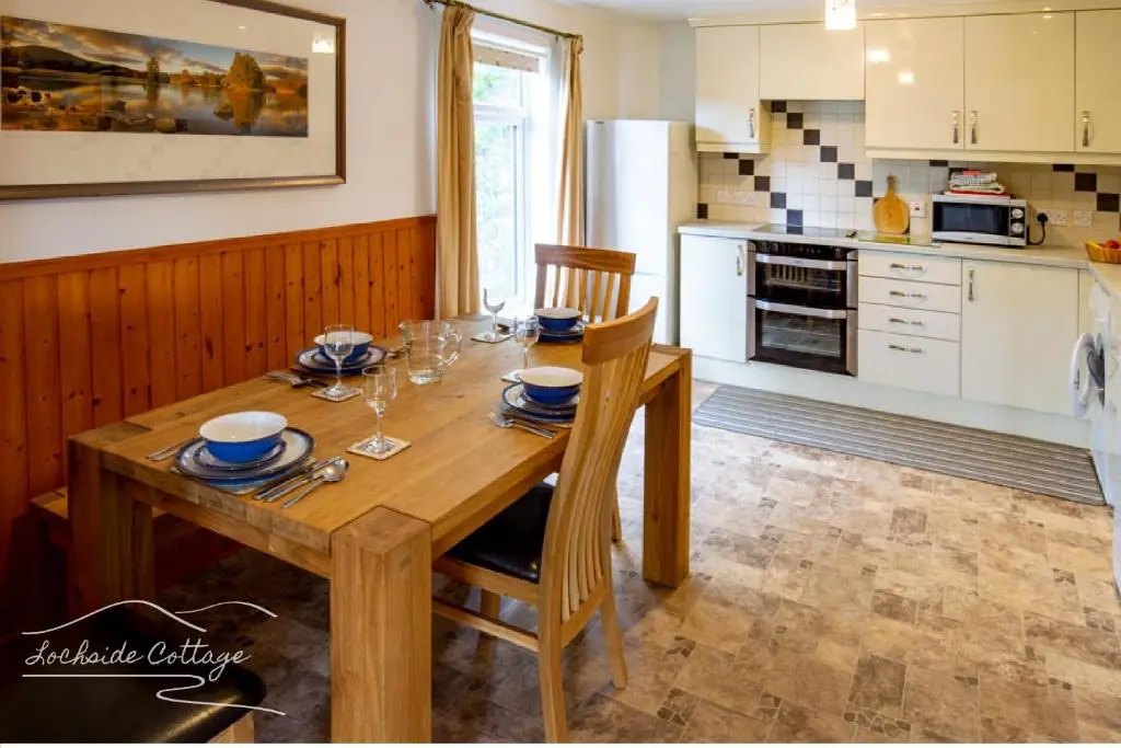 a kitchen with a wooden table with chairs and a kitchen with white cabinets at Lochside Cottage - near Aviemore in Aviemore