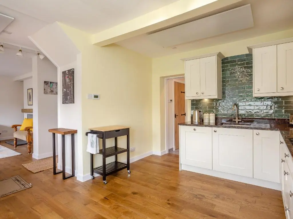a kitchen with white cabinets and wooden floors at Woodford - Cottage in Boat of Garten