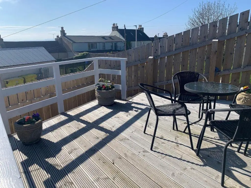 a patio with a table and chairs and a fence at Well Cottages in Portmahomack