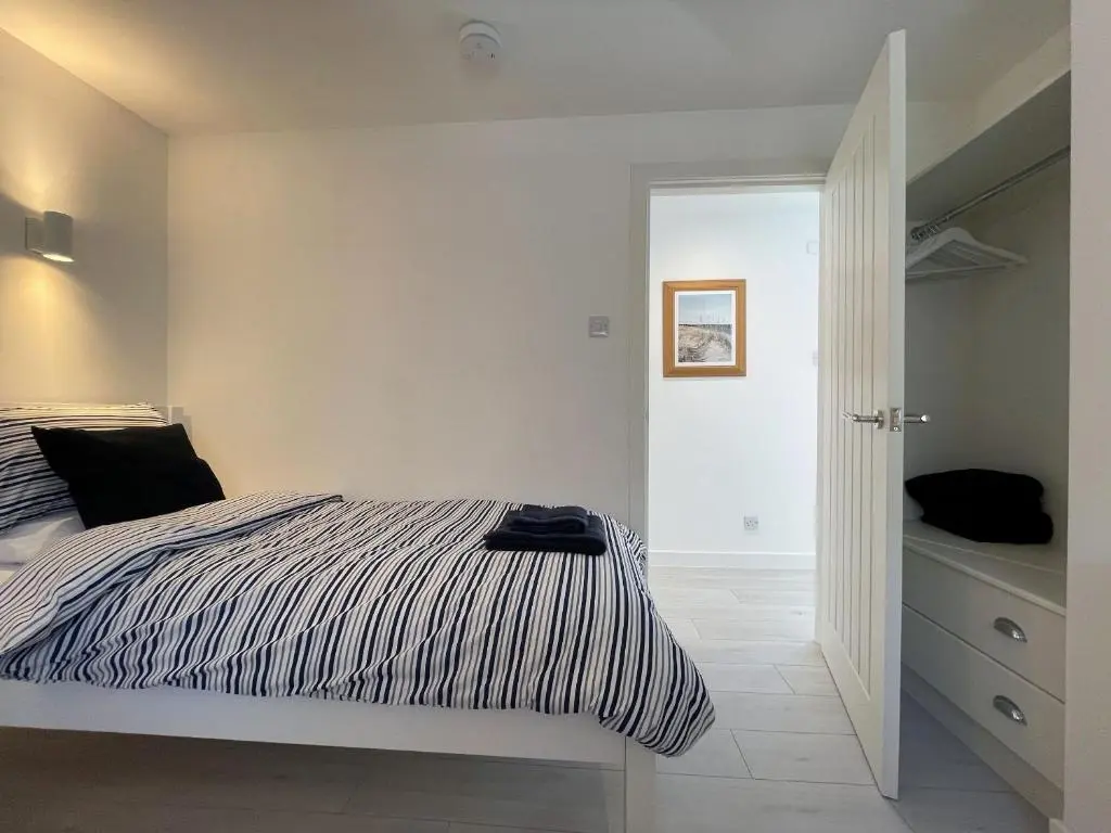 a white bedroom with a bed and a closet at Well Cottages in Portmahomack