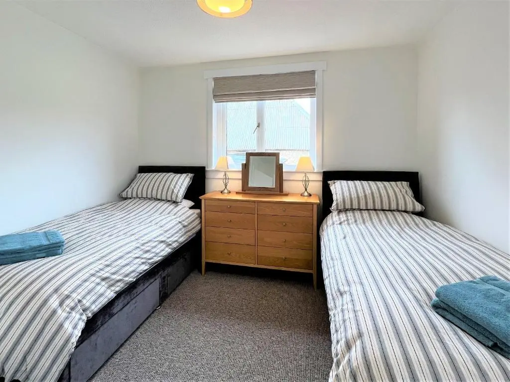 two beds in a room with a dresser and a window at Westerdales in Fort Augustus