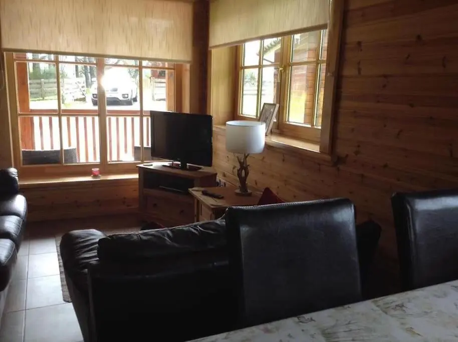 a living room with a couch and a tv and windows at Norwegian Log Cabin The Roe Deer -sauna & hot tub in Keith