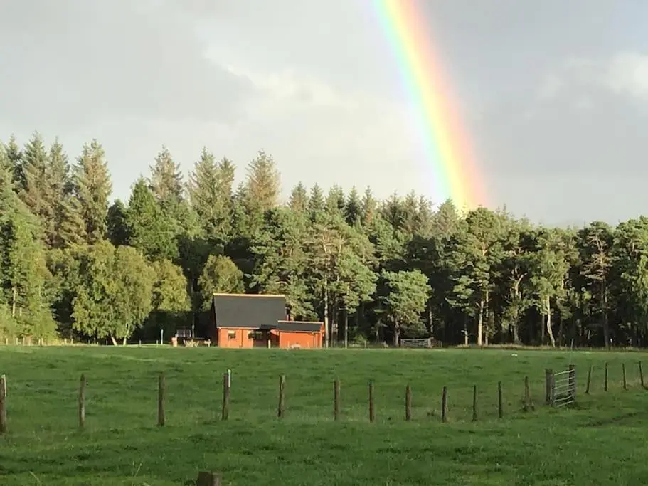 a rainbow in the sky over a field with a barn at Norwegian Log Cabin The Roe Deer -sauna & hot tub in Keith
