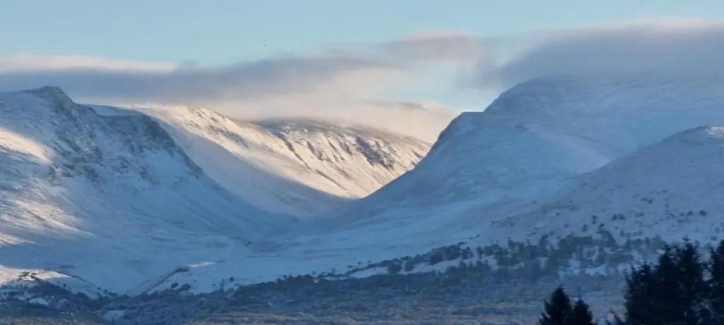 a snow covered mountain range with trees in the foreground at The Shelter Stone Cottage in Aviemore