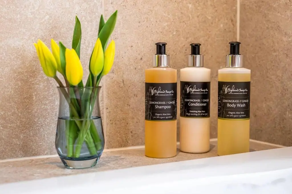 three bottles of shampoo and a vase with flowers on a shelf at Assynt House - Exclusive Use Holiday House in Dingwall