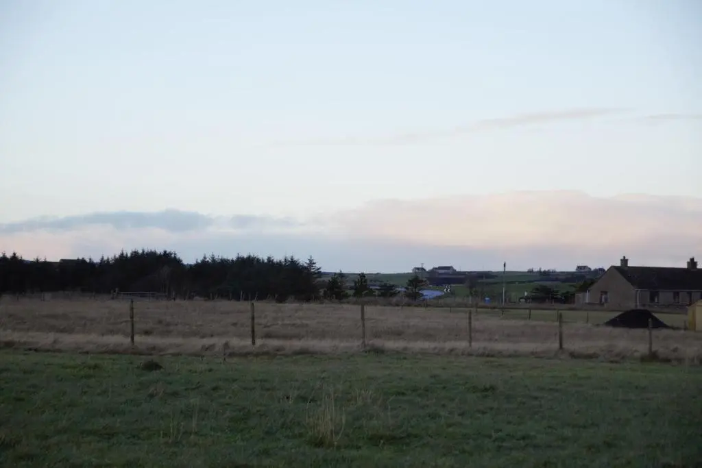 a field with a fence and a house in the distance at The Windy Roost in Occumster