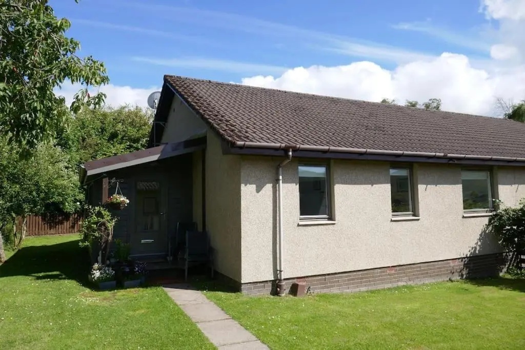 a small house with a green lawn in front of it at Stewart's Cottage, Aviemore Centre in Aviemore