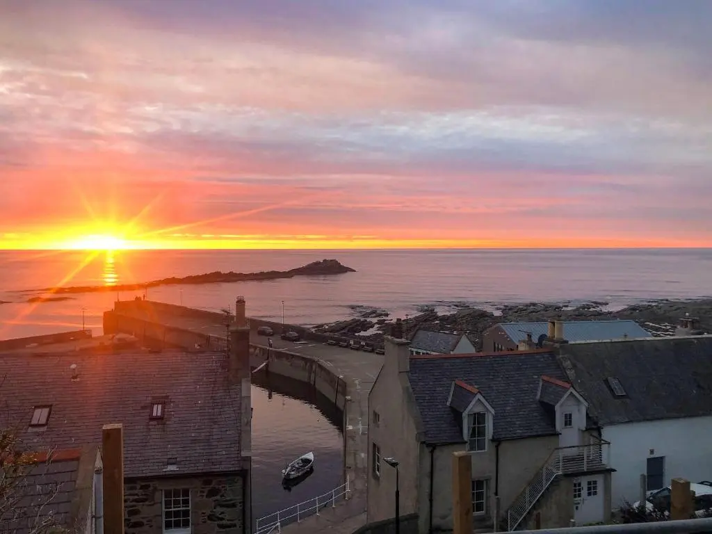 a sunset over the ocean and a town with houses at Harbour Road in Gardenstown