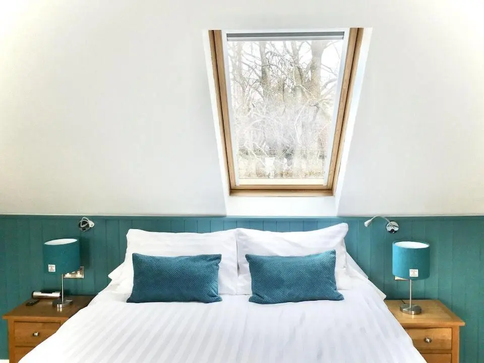 a bed with two blue pillows and a window at Baltinna West - by Where Stags Roar in Newtonmore