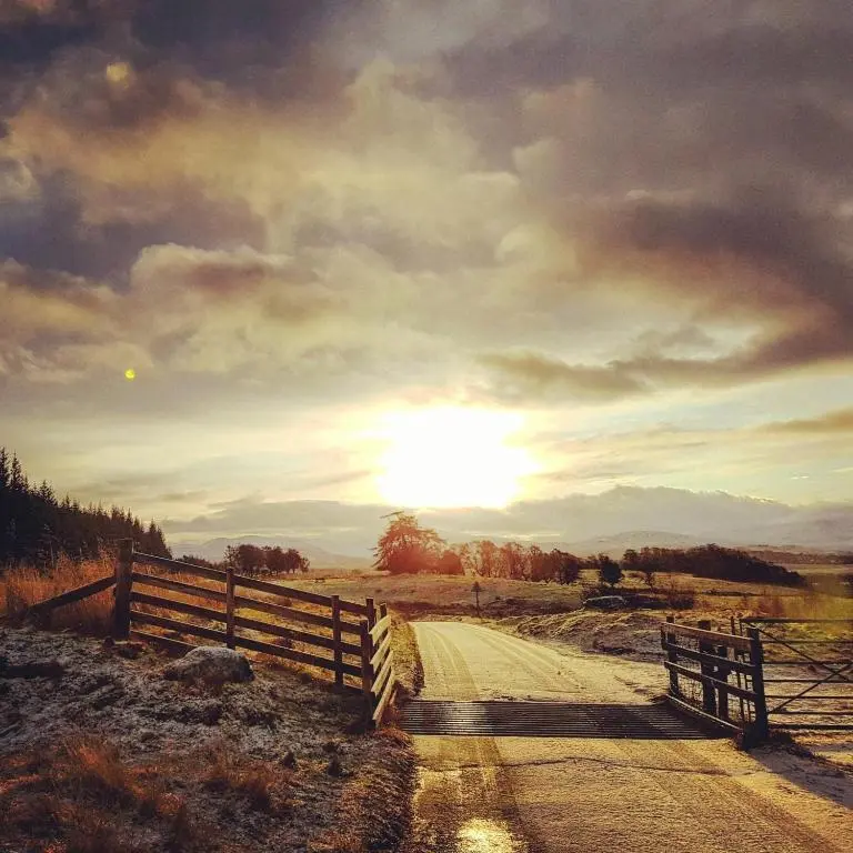 a dirt road with a fence and the sunset at Baltinna West - by Where Stags Roar in Newtonmore